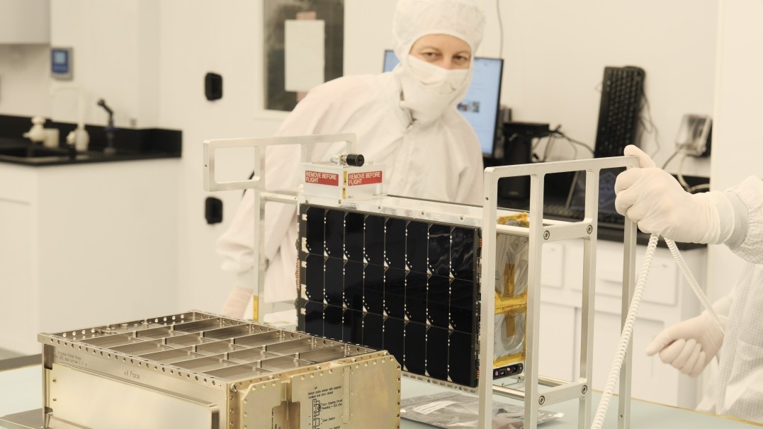 Image of ASU Professor Evgenya Shkolnik, principal investigator for the Star Planet Activity Research CubeSat mission, in white face mask and protective white clothing inspecting the space instrument as its being built in a clean room.