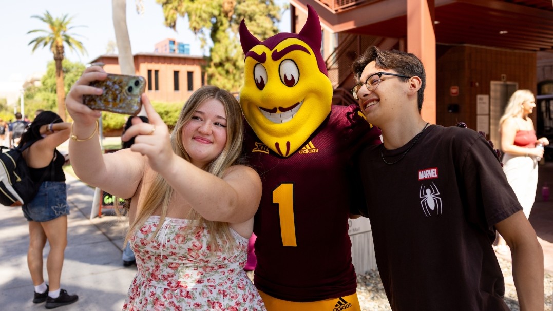 A male and female ASU student take a photo with Sparky, the ASU mascot 