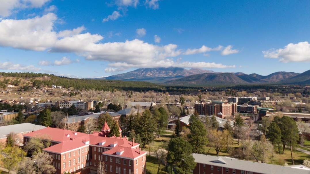 Aerial view of the NAU Flagstaff campus with buildings in the foreground and the San Francisco Peaks in the background 