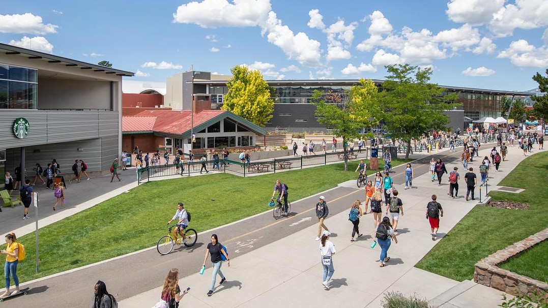 Students walking on the pedway path on the NAU campus with a building to the side and clouds in the sky