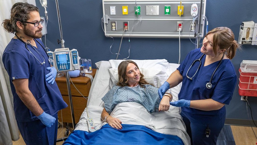 Two NAU nursing students in scrubs and protective gloves treat a patient.