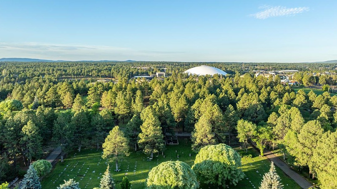 Aerial photo of the NAU campus with pine trees and mountains in the distance. 