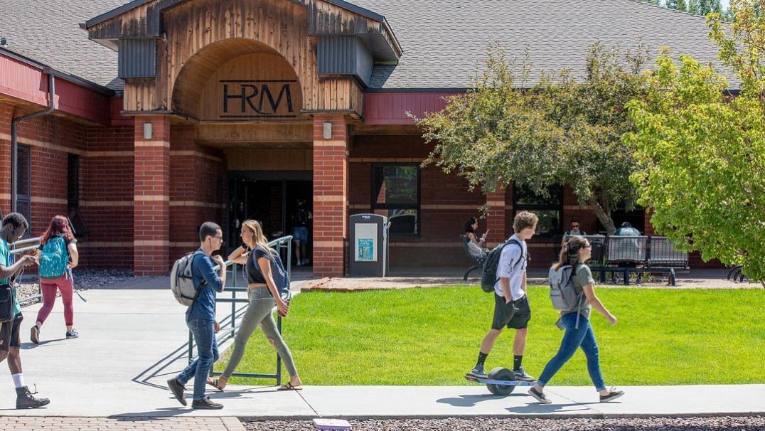 Photo of students walking on campus in front of a brick building 