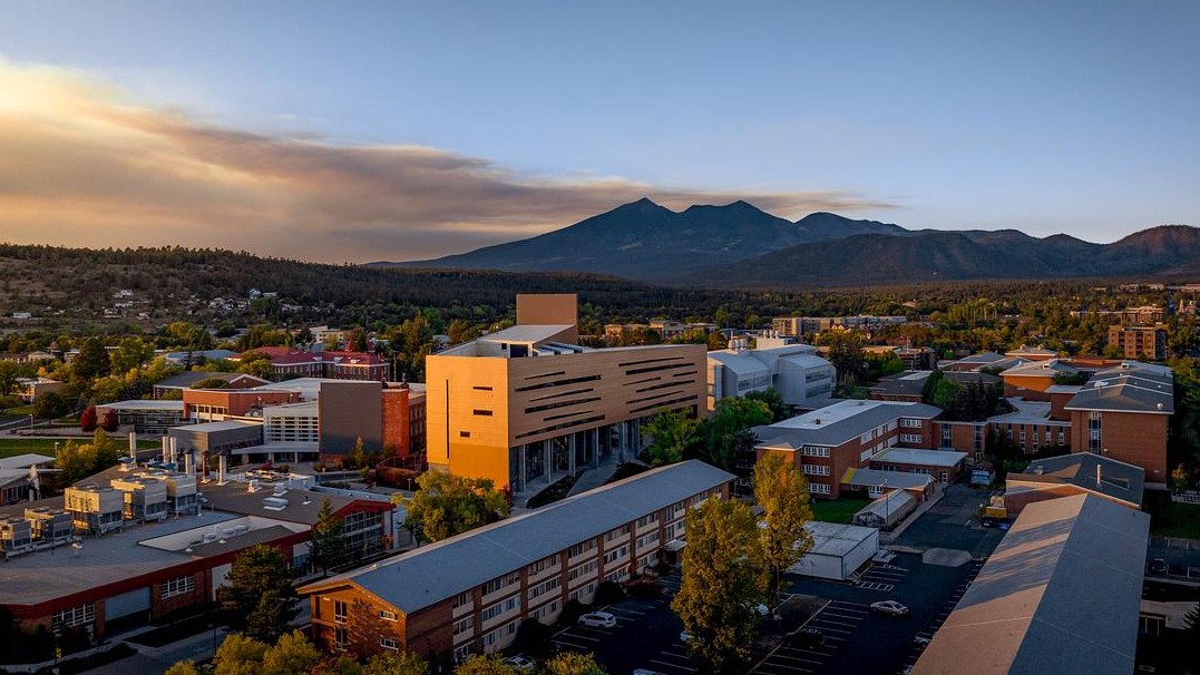 Aerial photo of the NAU campus at sunset with buildings in the foreground and the San Francisco Peaks in the background 