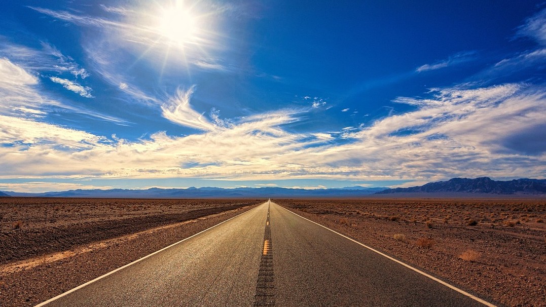 Photo of a deserted road with clouds in the sky, mountains in the distance and fluffy clouds in the sky.