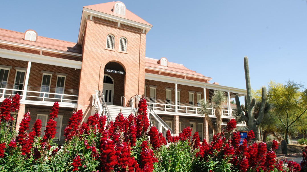 Photo of the Old Main building on the U of A campus with colorful flowers in the foreground. 