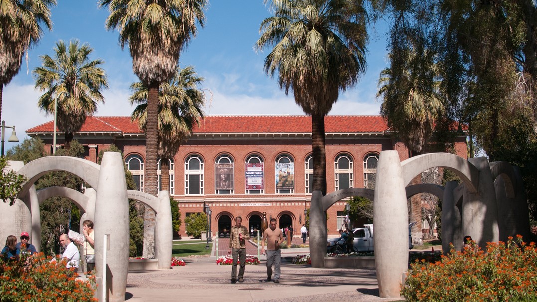 Two male students walking on campus in front of the Arizona State Museum. 