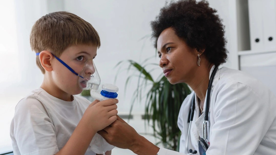 A female doctor is shown giving a breathing treatment to a young boy. 