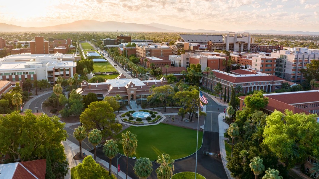 Aerial image of the U of A campus with the American flag in the foreground and Old Main and its fountain in the background. 