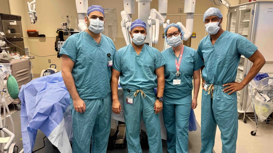 Four doctors in scrubs and facemasks are shown in an operating room. 