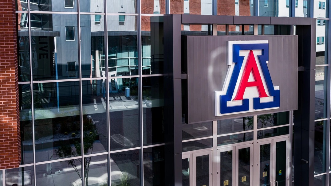 The University of Arizona "A" logo is pictured on the side of a building with reflective glass windows.