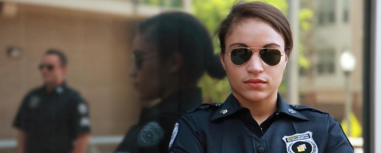 Image of a female officer in sunglasses looking at the camera with a male officer in the background 