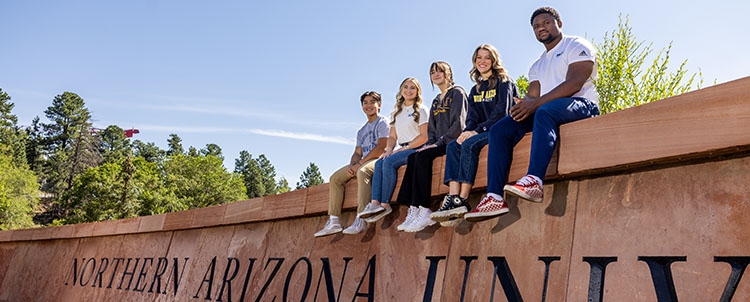 Photo of students sitting on a ledge above a sign that says Northern Arizona University