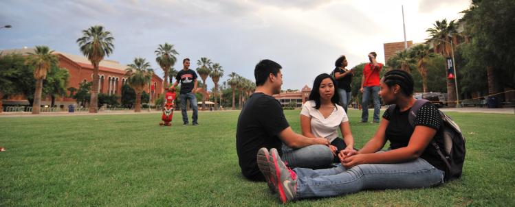Photo of two female students and a male student relaxing on the University of Arizona lawn 