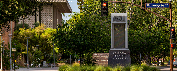 Image of an ASU sign on campus with a streetlight to the right, building to the left and trees and shrubbery in the image.