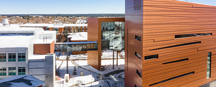 Photo of NAU campus with copper buildings in the foreground and snow on the ground. 