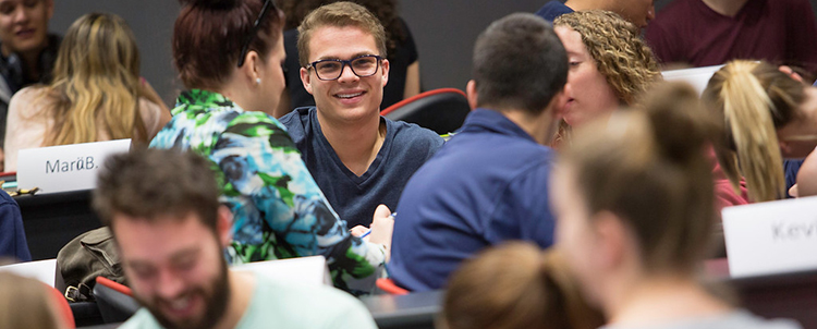 Photo of a smiling, male student at a table interacting with other seated students