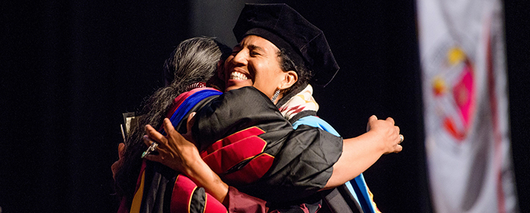 Photo of an Indigenous graduate hugging another person at graduation. 