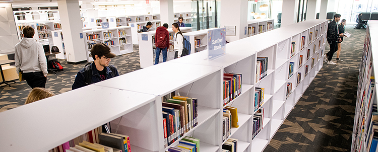 Photo of the interior of a library with students studying and shelves of books 