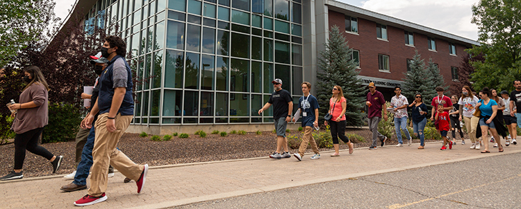 Image of NAU's campus and students taking a campus tour, walking in front of a building outside 