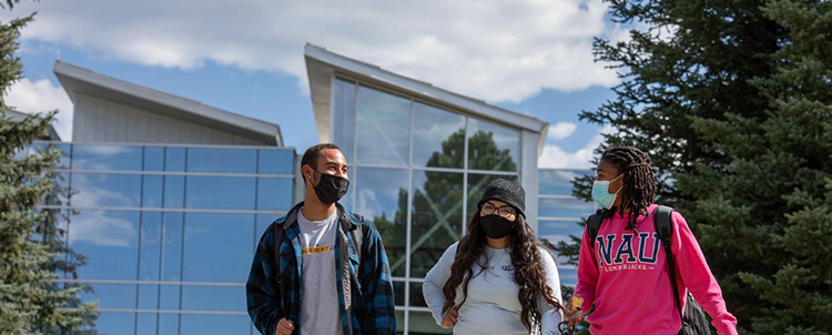 Photo of three NAU students outside of a building. All of the students have on facemasks. 