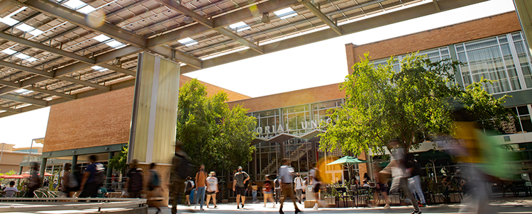 Photo of students walking outside of the Memorial Union on the ASU Tempe campus with solar panels on shade structures in the foreground