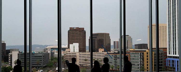 Photo of the Phoenix skyline from a large window with people in front of it 