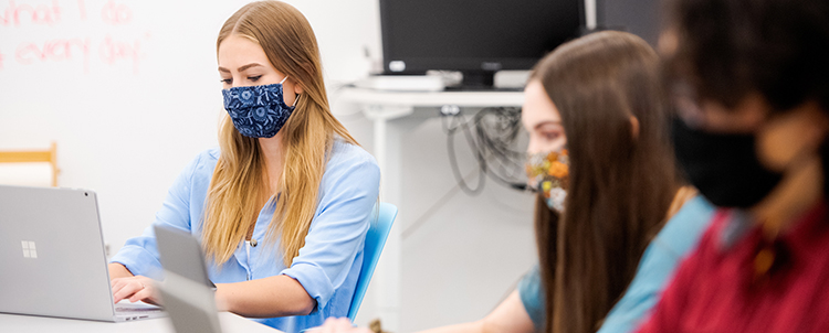 Photo of three students in facemasks working on computers in class 