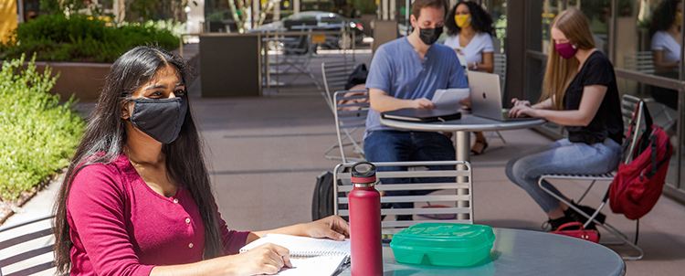 Students studying outside on campus at tables with facemasks on  